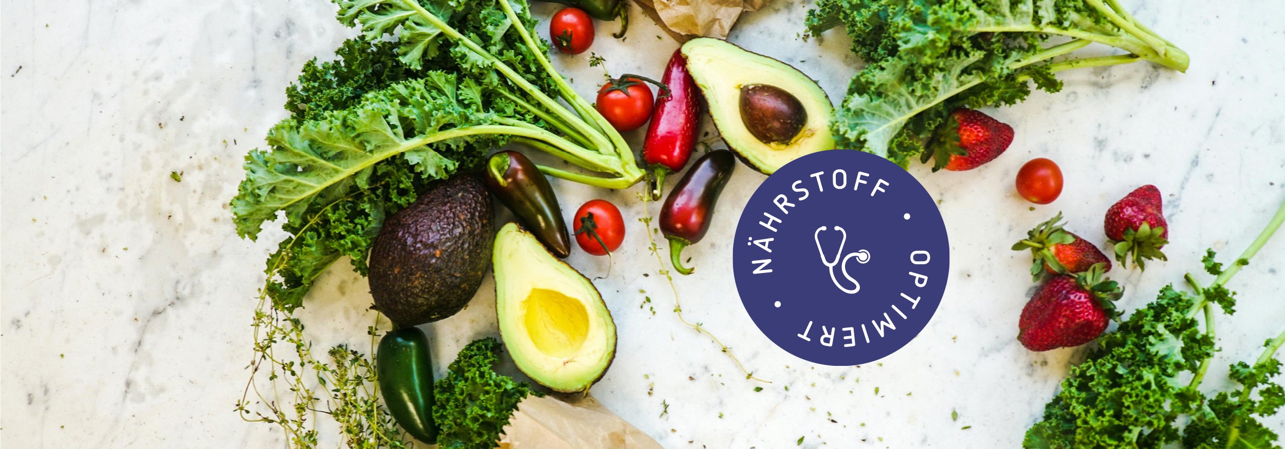 Vielfältige, vegane Auswahl aus grünem und rotem Gemüse und Obst auf einer Marmorplatte in der Küche verbildlicht einen gesunden Einkauf.